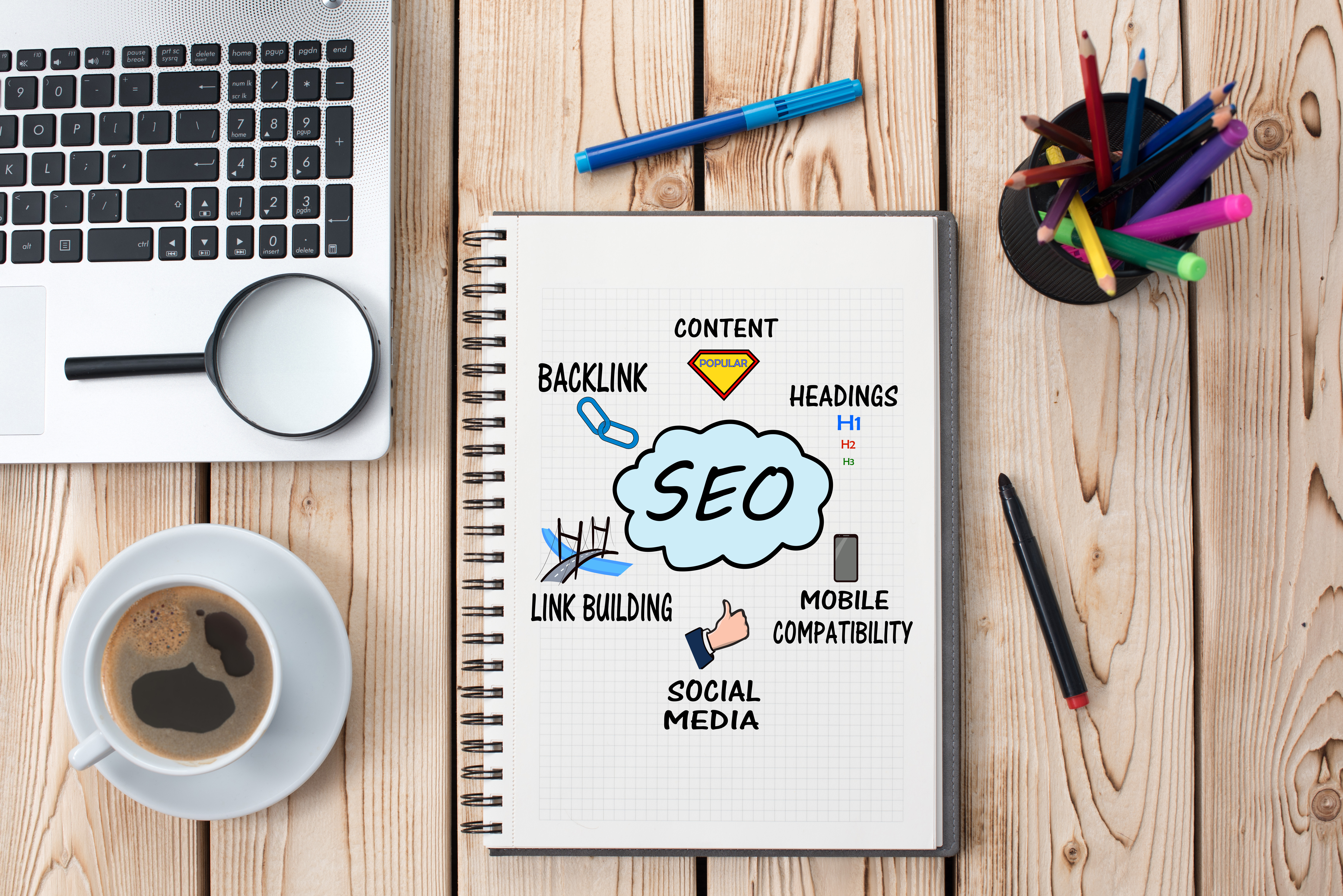 desktop with a laptop, a cup of coffee, and an open notebook showing SEO themed notes